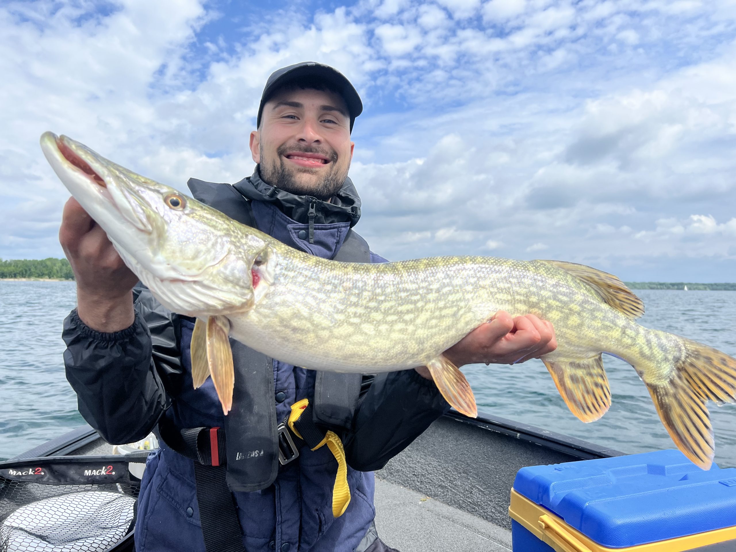 Un pêcheur heureux ! Adrien souriant tenant un gros brochet fraîchement pêché au Lac du Der, lors d'une sortie de pêche guidée mémorable.