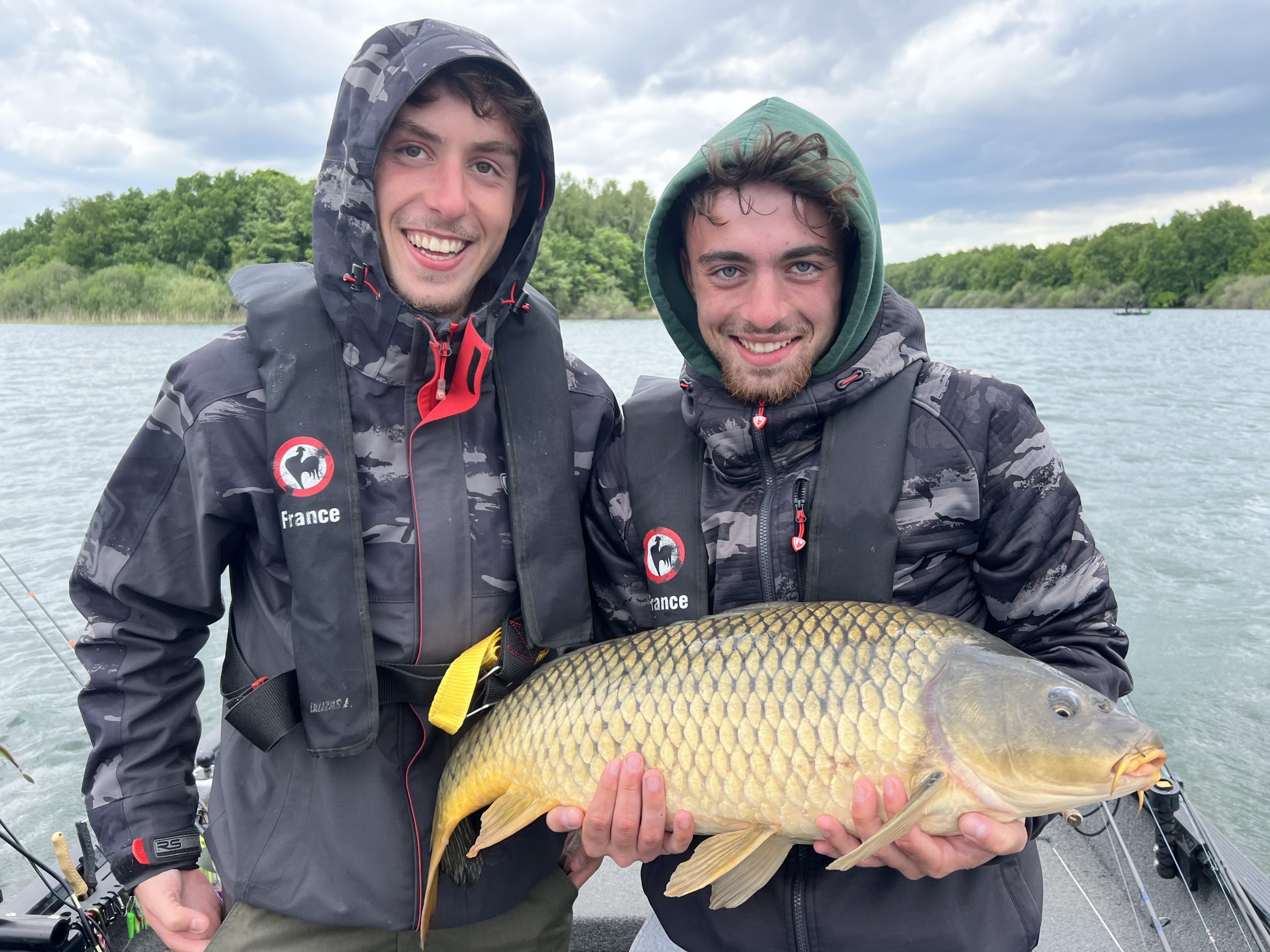 Belle carpe prise par Andrea Au leurre Sur cette photo prise au bord du Lac du Der, Andréa affiche un grand sourire en tenant fièrement la superbe carpe qu’il vient tout juste de pêcher, sous le regard complice de Pierre. Un moment de joie et de réussite qui illustre parfaitement la passion partagée et l’intensité de cette journée au grand air.